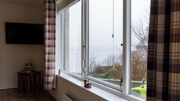 A room with a large window, a small table with a basket, and a television mounted on the wall. - Central Lerwick holiday apartment (Lerwick)