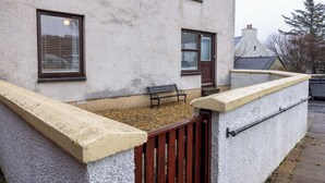 A building with a textured exterior, a wooden bench, a small door, and a window with blinds. - Central Lerwick holiday apartment (Lerwick)
