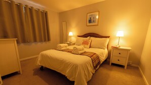 A neatly made bed with white linens, two bedside tables with lamps, and a large window with curtains. - Central Lerwick holiday apartment (Lerwick)
