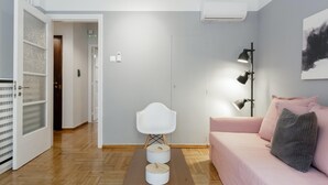 A modern living room with a wooden floor, a white sofa with pink cushions, a white chair, and a black floor lamp. - Chic and Cosy Flat in Plaka (Athina)