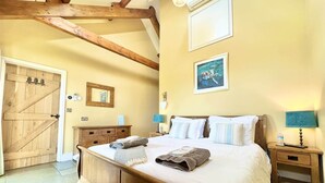 Een slaapkamer met een houten bed, een houten garderobe, een spiegel, een nachtkastje met een lamp, en een deur met een rustieke uitstraling.