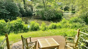 Een houten terras met tafel en stoelen, uitkijkend op een vijver omringd door weelderige begroeiing.