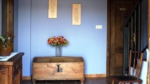 Una habitación con un cofre de madera, un jarrón con flores y dos cuadros en la pared.