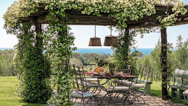 An outdoor dining area with a pergola covered in greenery, a table set with food, and a view of the sea. - Villa Il Meluccio 12, Emma Villas (Castellina Marittima)