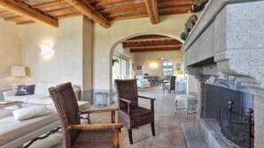 A spacious lounge area with a fireplace, wicker furniture, and a dining area in the background. - Villa Il Meluccio 12, Emma Villas (Castellina Marittima)