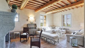 A cozy living room with a fireplace, wicker furniture, and a stone accent wall. - Villa Il Meluccio 12, Emma Villas (Castellina Marittima)