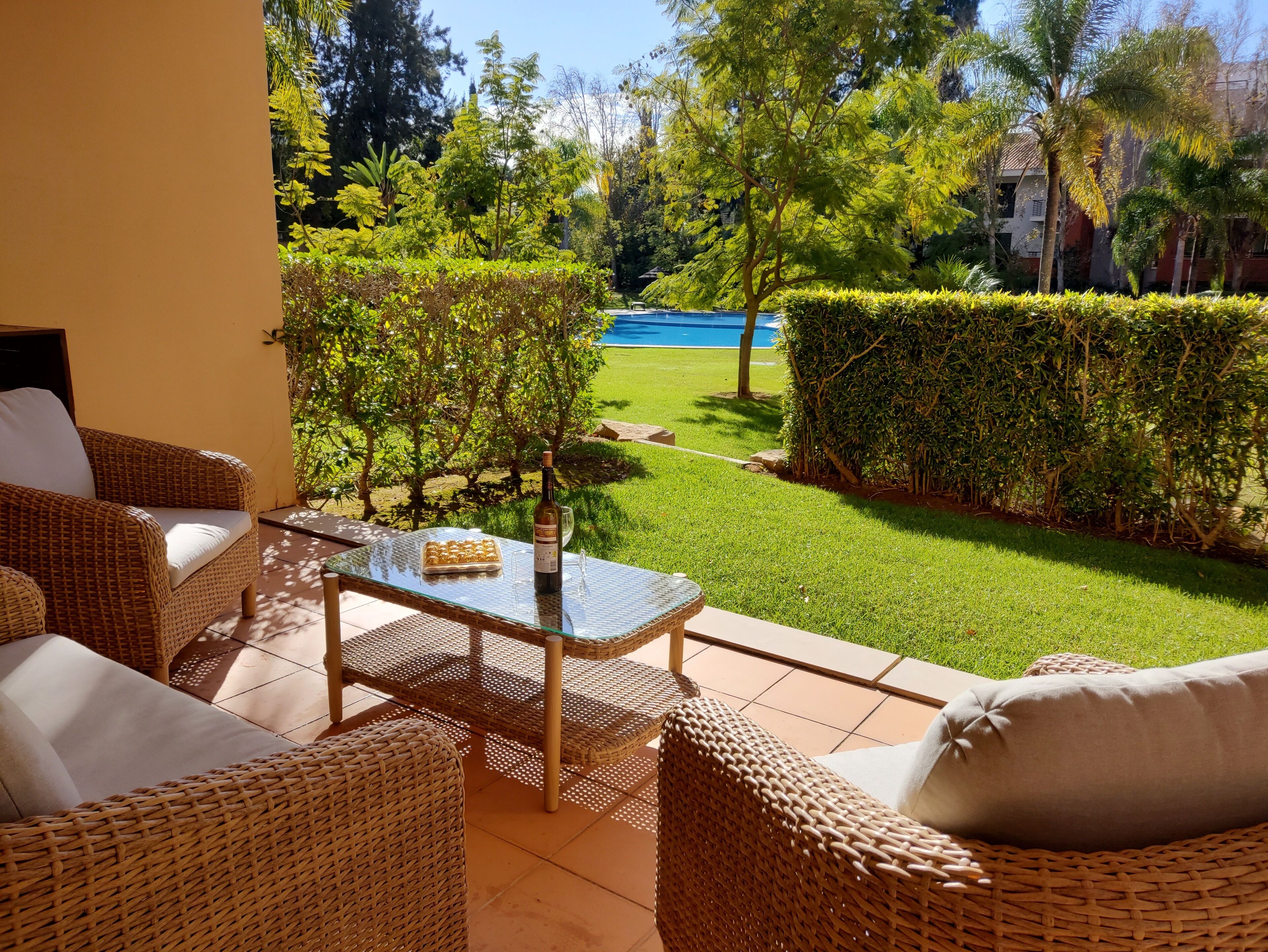 Eine Terrasse mit Korbmöbeln, einem Glastisch und einer Weinflasche.