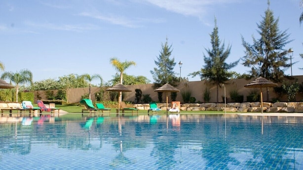 A swimming pool with tiled flooring, surrounded by lounge chairs and umbrellas, with trees and a clear sky in the background. - NEWLY REFRUB LUX 2 bed Apart (Sleeps 4) FREE Wi-Fi  Close to Marina Beach & Golf (Vilamoura)