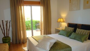 A hotel room with a bed, a nightstand, a lamp, a window with curtains, and a view of the outdoors. - NEWLY REFRUB LUX 2 bed Apart (Sleeps 4) FREE Wi-Fi  Close to Marina Beach & Golf (Vilamoura)