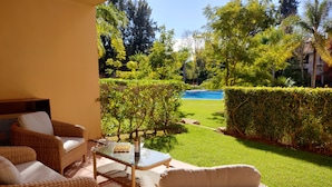 A patio area with wicker furniture, a glass table, and a view of a swimming pool and garden. - NEWLY REFRUB LUX 2 bed Apart (Sleeps 4) FREE Wi-Fi  Close to Marina Beach & Golf (Vilamoura)