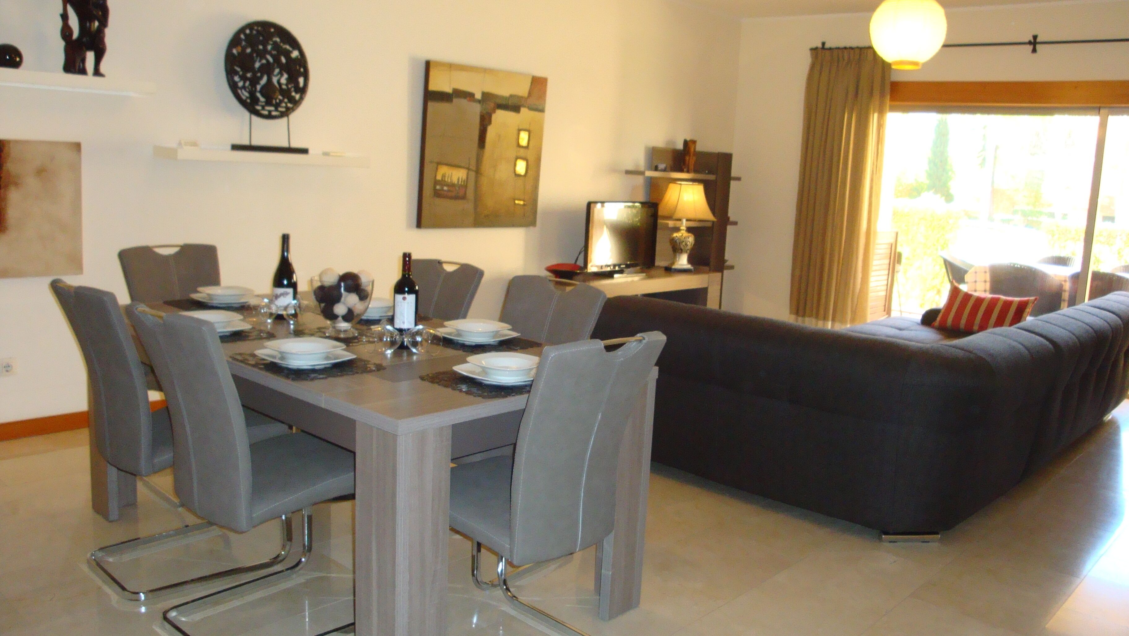 A dining area with a table set for four, a sofa, and a TV.