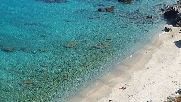 Une plage à l’eau turquoise et limpide, bordée de formations rocheuses.