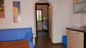Une pièce avec une table en bois, un canapé bleu, un coin cuisine avec des placards et un sol carrelé.