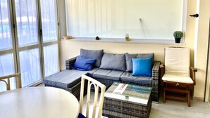 Ein gemütliches Zimmer mit einer Couch, einem Sessel, einem Tisch und einem Fenster mit Jalousien.