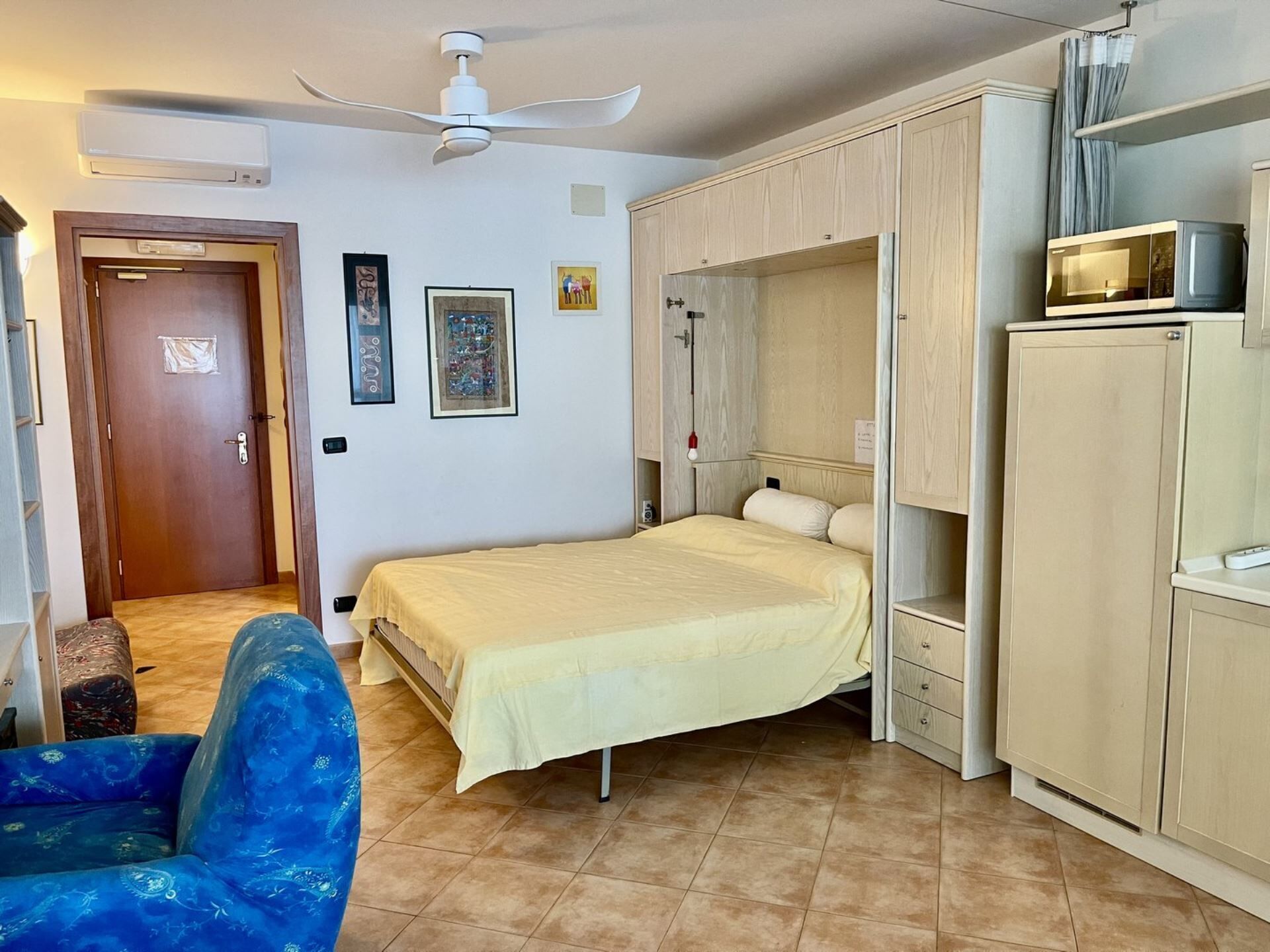 A bedroom with a bed, a wardrobe, a chair, and a ceiling fan.