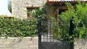 A stone building with a metal gate, a balcony with a railing, and lush greenery.