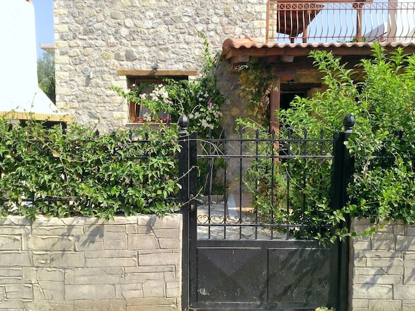A stone building with a metal gate, a balcony with a railing, and lush greenery.