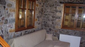 A stone-walled room with a sofa, two wooden-framed windows, and a radiator.