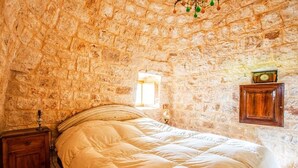 A bedroom with a stone wall, a bed, a nightstand, and a wall clock. - Trullo in the woods, a few steps from a hiking and cycling trail (Cisternino)