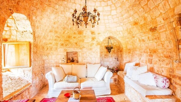 A cozy room with a stone wall, a white sofa, a wooden coffee table, and a chandelier. - Trullo in the woods, a few steps from a hiking and cycling trail (Cisternino)