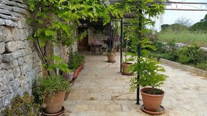 A stone-paved patio with potted plants and a pergola structure. - Trullo in the woods, a few steps from a hiking and cycling trail (Cisternino)