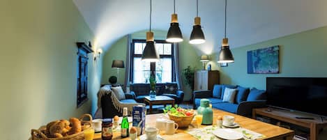 Un salón acogedor con una mesa de comedor lista para el desayuno, un sofá y un televisor.
