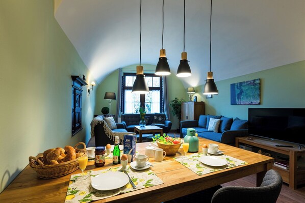 A cozy living room with a dining table set for breakfast, a sofa, and a TV. - Vacation in the Harz Mountains the special ****Holiday apartments Burggraf im Zwinger Goslar (Goslar)