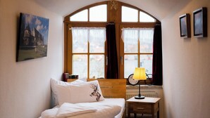 A bedroom with a bed, a nightstand, a lamp, a window with curtains, and a painting on the wall. - Vacation in the Harz Mountains the special ****Holiday apartments Burggraf im Zwinger Goslar (Goslar)