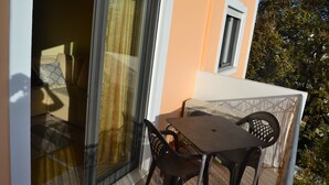 En balkong med ett bord och stolar, en skjutdörr i glas och ett litet fönster.