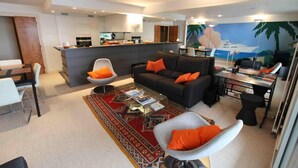 A modern living room with a sofa, armchairs, a coffee table, and a dining area.