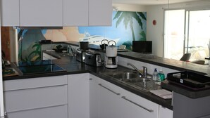 A modern kitchen with white cabinets, a black countertop, a coffee maker, a kettle, and a sink.