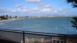 A coastal view from a window overlooking a beach, a clear sky, and a distant shoreline with buildings.