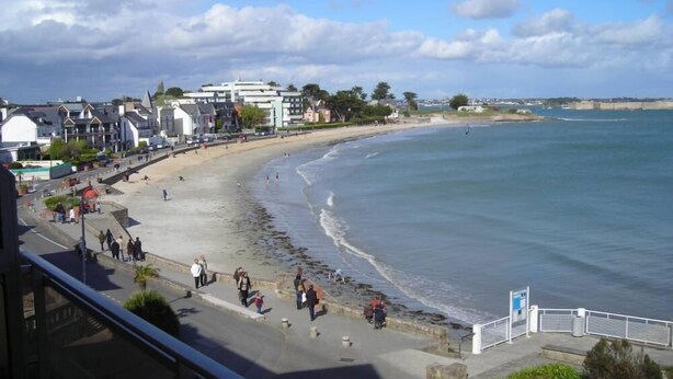 A coastal town with a sandy beach, promenade, and buildings along the shore.