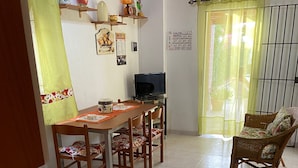 A dining area with a table, chairs, a television, and a wicker chair.