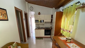 A cozy dining area with a wooden table and chairs, a sofa with floral cushions, and a kitchen in the background.