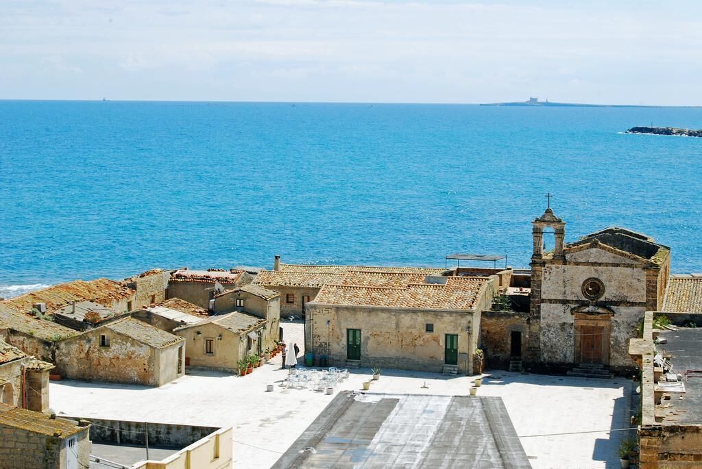 A coastal village with traditional stone buildings, a central church, and a view of the sea.