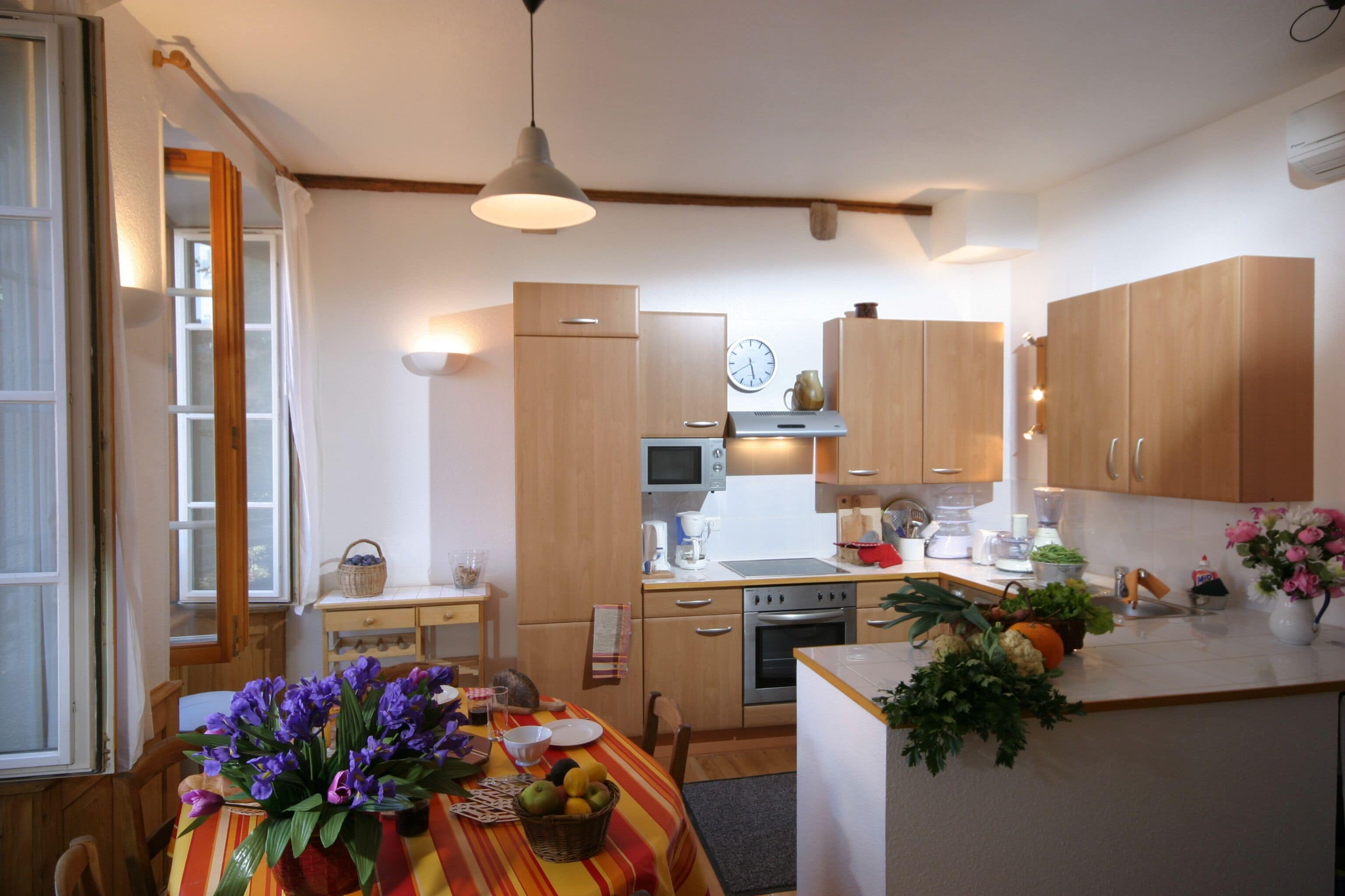 A compact kitchen with wooden cabinets, a dining table with a striped tablecloth, and a variety of kitchen appliances.