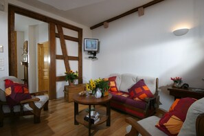 A cozy living room with a wooden floor, a sofa with colorful cushions, a coffee table with books and a vase of flowers, and a television mounted on the wall. - Apartment La COLLEGIALE in the old town with free parking (Colmar)