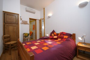 A bedroom with a wooden bed, a nightstand with a lamp, a chair, and a wooden wardrobe. - Apartment La COLLEGIALE in the old town with free parking (Colmar)
