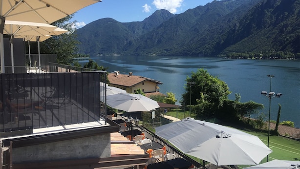 A terrace with outdoor seating and umbrellas overlooking a lake with mountains in the background. - Directly from the owner (Tre Capitelli)