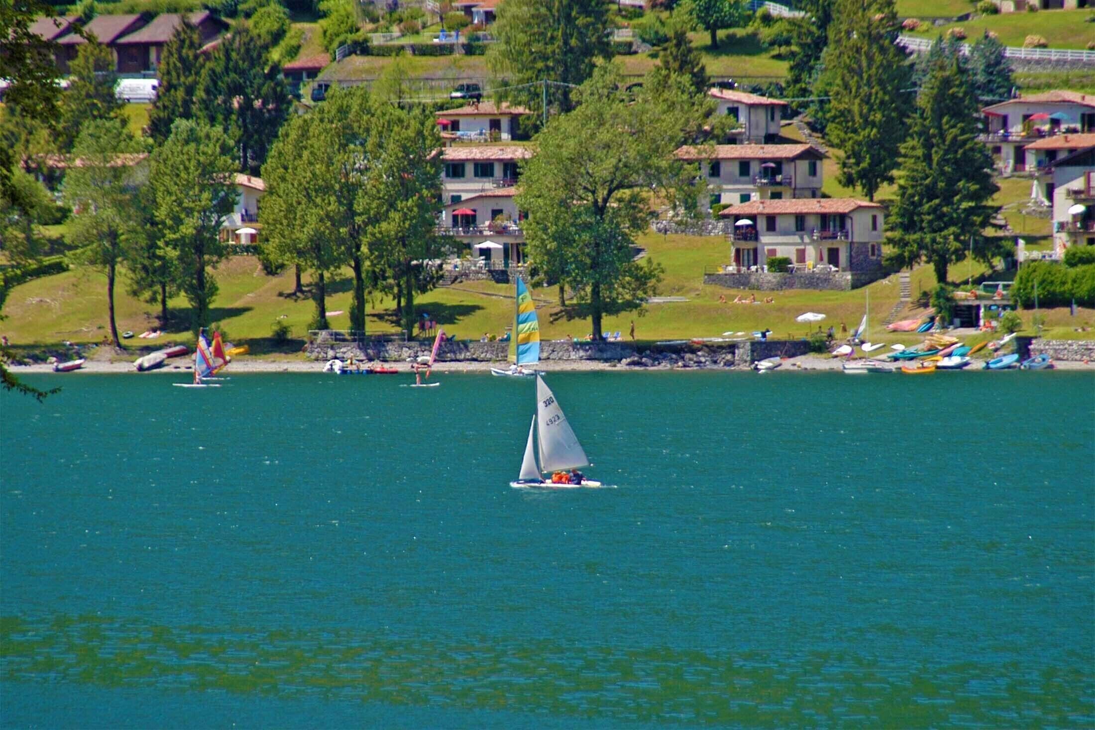 A sailboat on a calm lake with houses in the background.