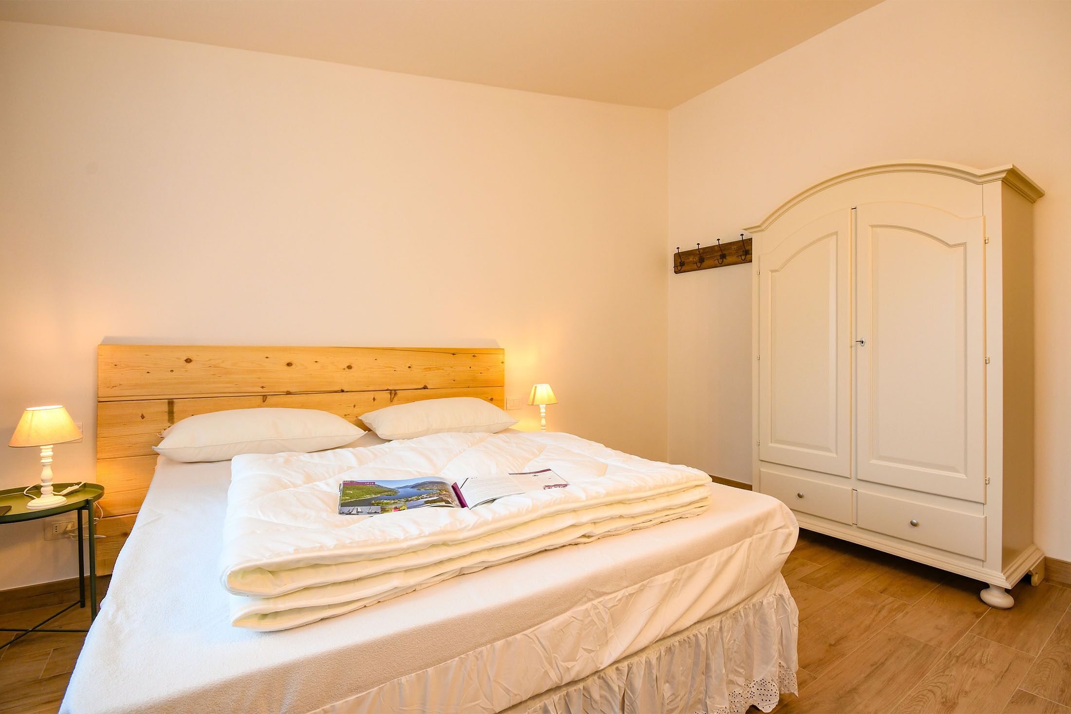 Een netjes opgemaakt bed met een witte dekbedovertrek, een houten hoofdbord en twee bedlampjes.