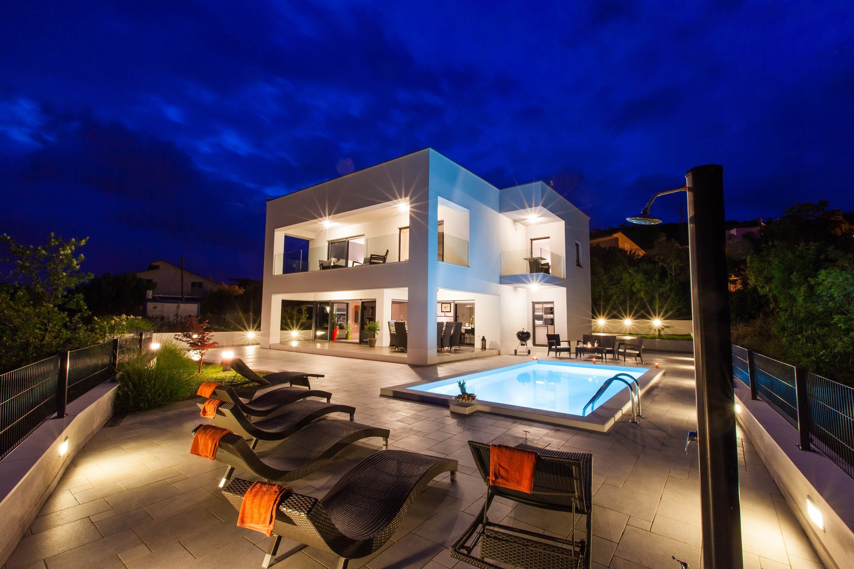 A modern two-story house with a swimming pool, outdoor seating, and a well-lit patio area.