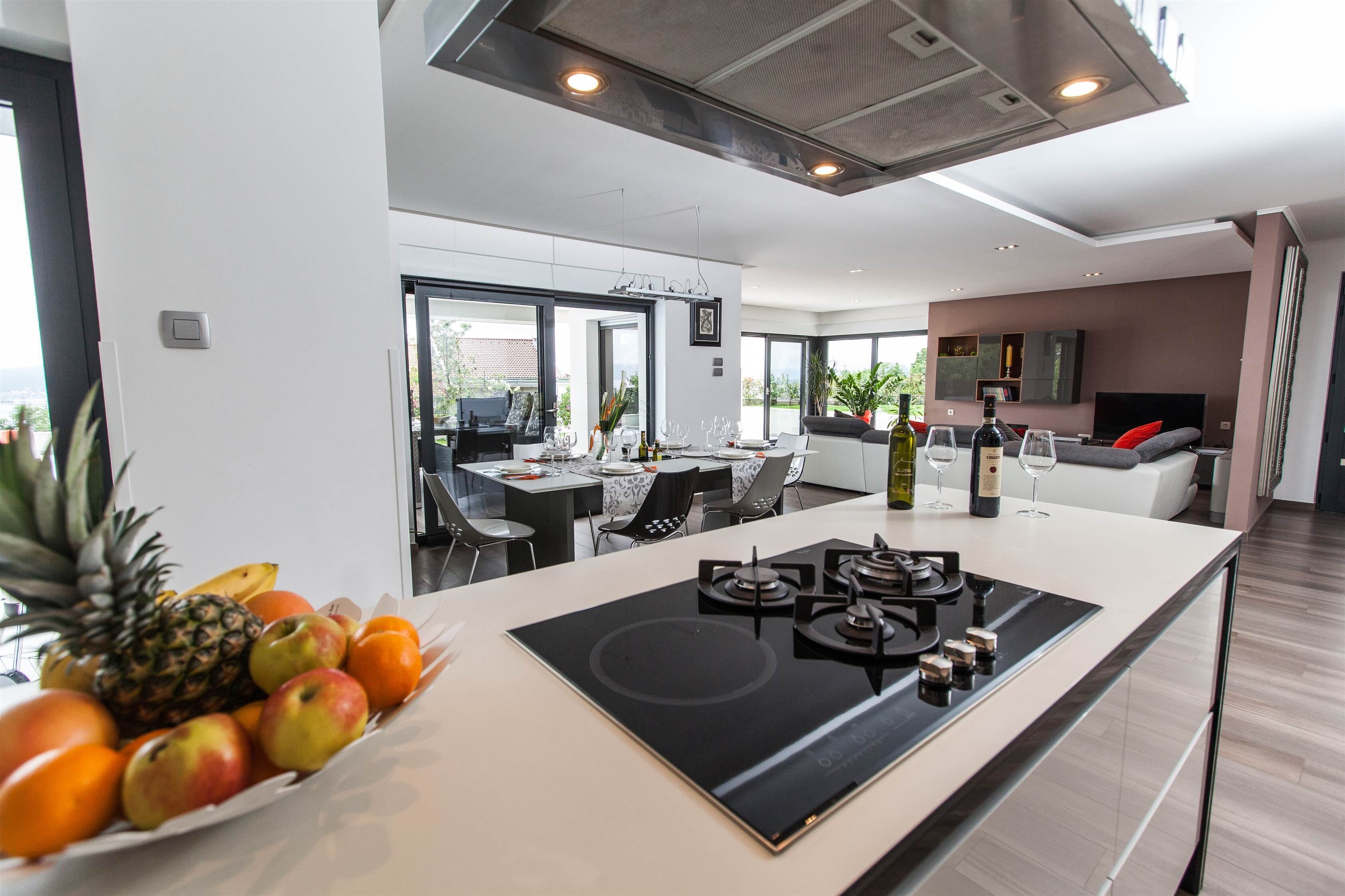 Una cucina moderna con isola centrale, zona pranzo e angolo salotto con divano e televisore.