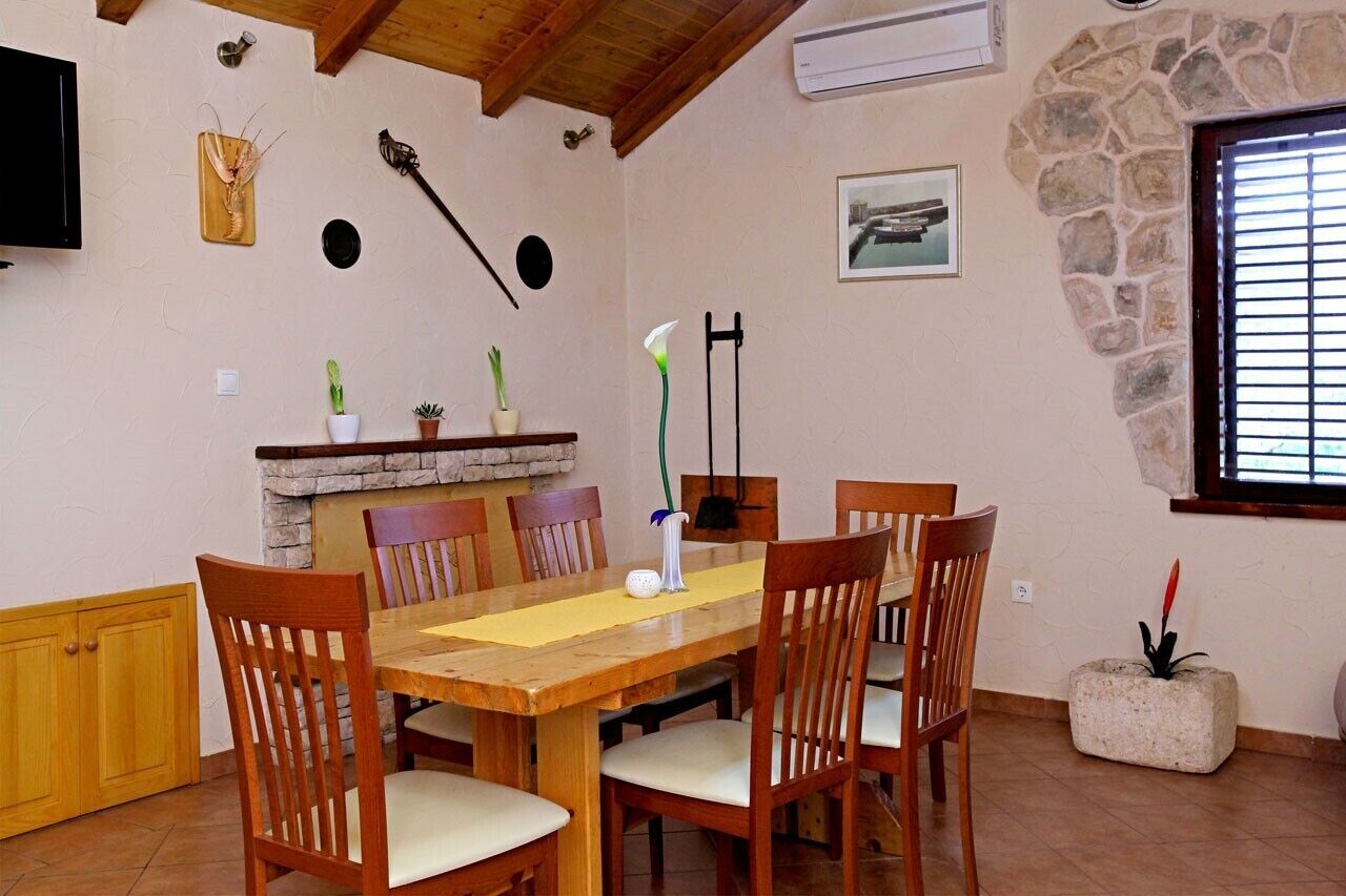 Un comedor con una mesa y sillas de madera, chimenea de piedra y pared de piedra.