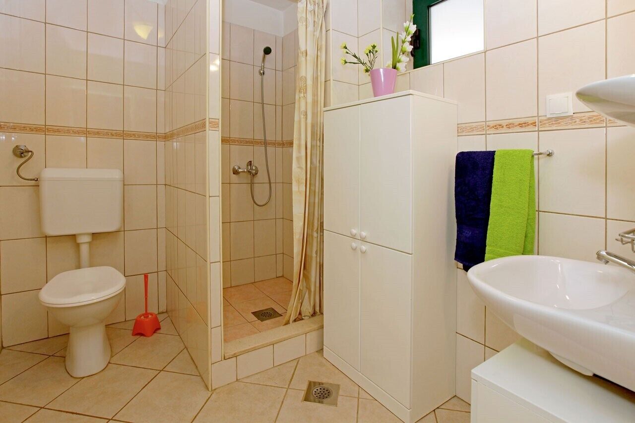 A bathroom with a toilet, shower, sink, and cabinet.