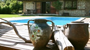 A rustic outdoor setting with a stone building, a swimming pool, and two pottery items on a wooden deck.