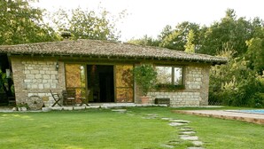 A stone house with a tiled roof, a paved driveway, and a stone pathway leading to the entrance.