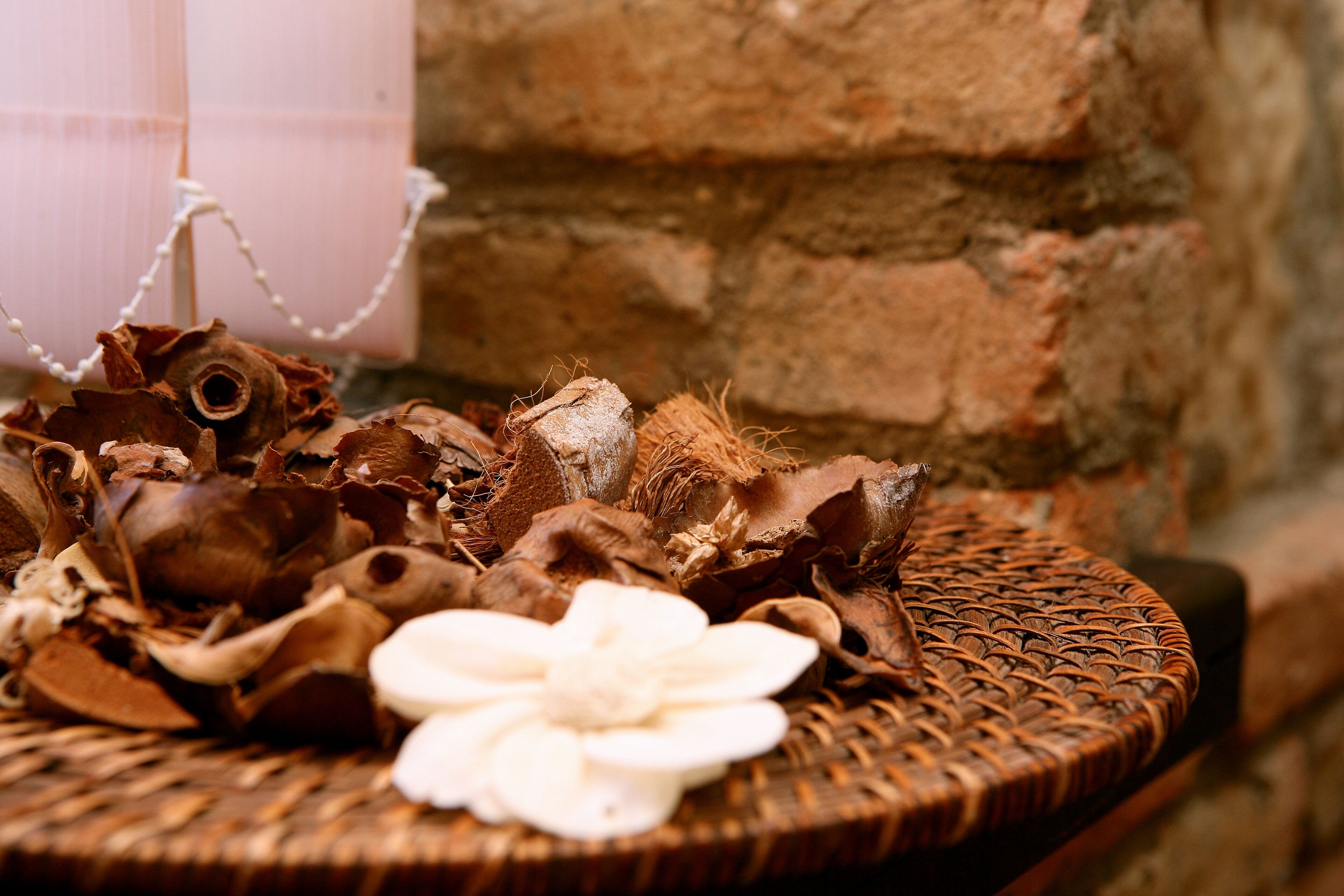 A wicker basket with dried leaves and a white flower on a round table against a brick wall.