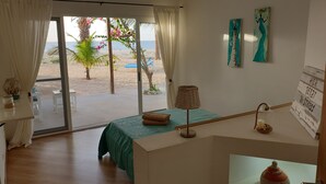 Une chambre avec vue sur la plage, un lit recouvert d’une couverture verte, une petite table avec une lampe et un mur orné de deux tableaux.